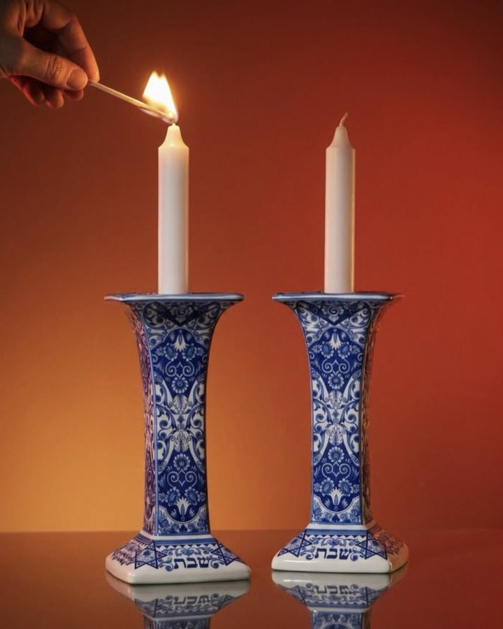 Blue and white Shabbat candlesticks being lit against a warm orange wall