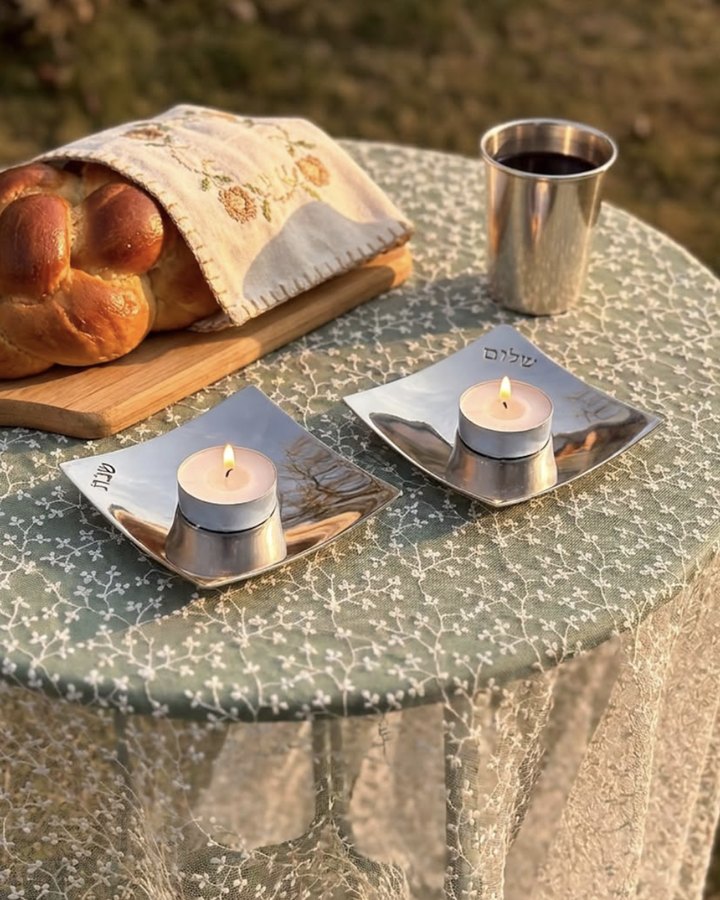 Shabbat tealight holders, challah and a kiddush cup on a garden table at sunset