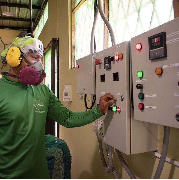 A Wiñak worker in protective gear operating the processing plant's control panel